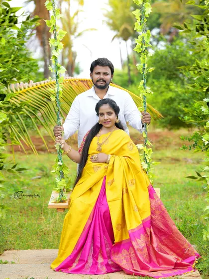 A vibrant outdoor portrait of a couple on our floral swing. The mother-to-be is wearing a bright yellow and pink silk saree that radiates joy.
