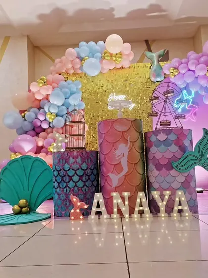 An enchanting mermaid theme for a 6th birthday party. This setup captures the magic of the sea with a shimmering gold backdrop, pastel balloon garlands, mermaid tail cutouts, and a large light-up number '6'.