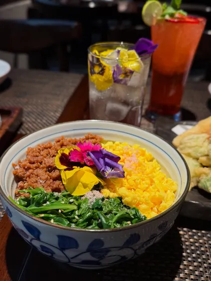 Our Spring Donburi from the Sakura menu. This colorful rice bowl is topped with seasoned ground chicken, fluffy scrambled eggs, and fresh spinach, adorned with edible flowers.