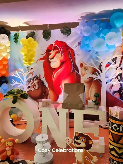 An indoor Lion King setup for a first birthday, featuring a dramatic backdrop of Pride Rock and many jungle animal props.