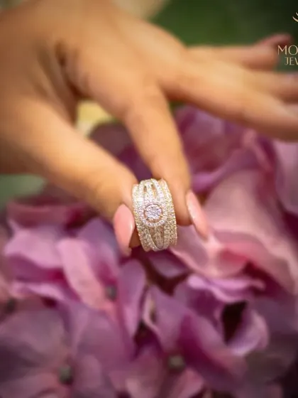 A magnificent diamond cluster ring, held against a backdrop of flowers. This image captures the romance and celebratory nature of gifting and wearing fine jewellery.