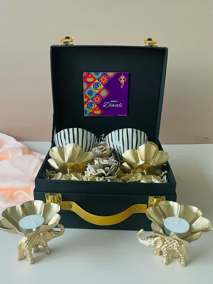 This view shows the complete set: the black suitcase box, two striped ceramic cups, and the matching golden elephant t-light holders, creating a cohesive and premium gift.