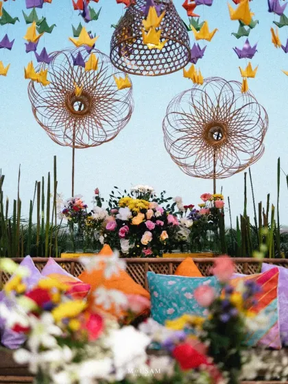 A vibrant and colorful Mehendi or Haldi seating area. The mix of origami cranes, bamboo details, and brightly colored cushions creates a festive and photogenic space, perfect for capturing joyful moments.