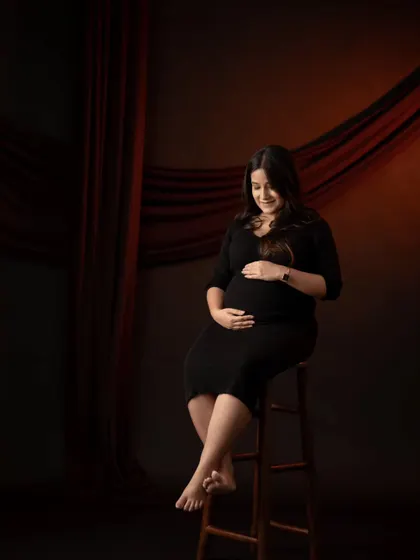 A classic, moody studio portrait. The dramatic lighting highlights the mother-to-be's profile and her gentle expression as she looks down at her bump.