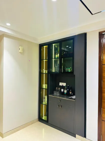 A compact yet elegant mini-bar built into a niche, featuring glass-fronted cabinets with internal lighting and a practical countertop for mixing drinks.