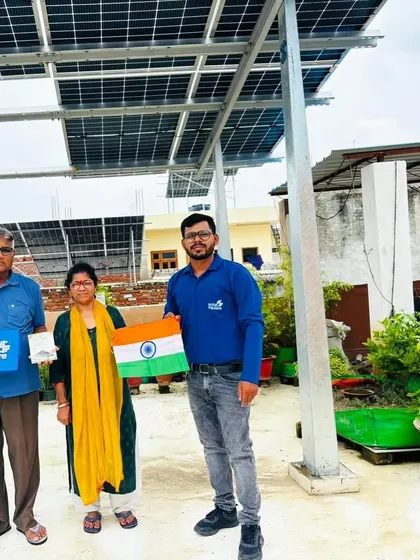 An elderly couple with our team member, proudly holding the Indian flag under their new solar panels.