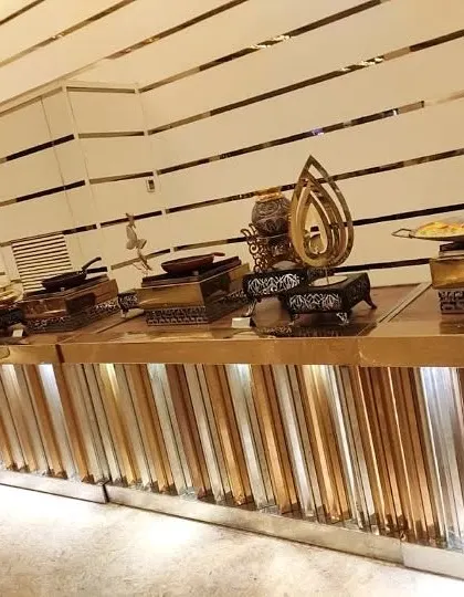 A modern and chic buffet counter with a gold and white striped design. The warm under-lighting highlights the metallic finish of the counter and the ornate serving dishes.