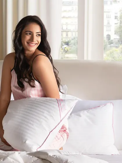 A bright and cheerful shot for a pillow collection. The natural window light and the model's happy expression create a fresh, positive feeling that is perfect for a morning-themed lifestyle shoot.