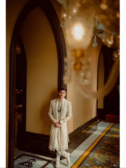 A stylish portrait of the groom in a majestic, arched hallway. The architecture and lighting create a sense of grandeur and sophistication.