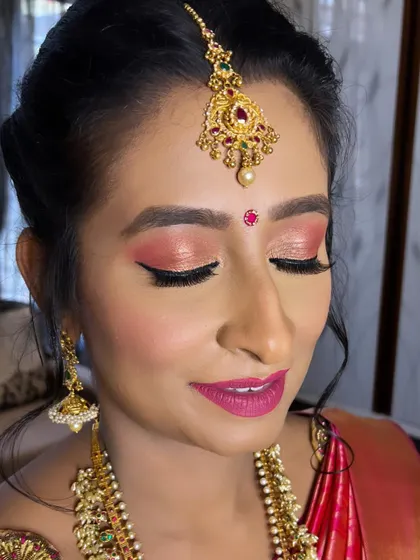 A vibrant Muhurtham look for a family wedding. This makeup features shimmery pink eyeshadow with winged liner and a bold pink lip, perfectly matching the client's silk saree and Guttapusalu haram.