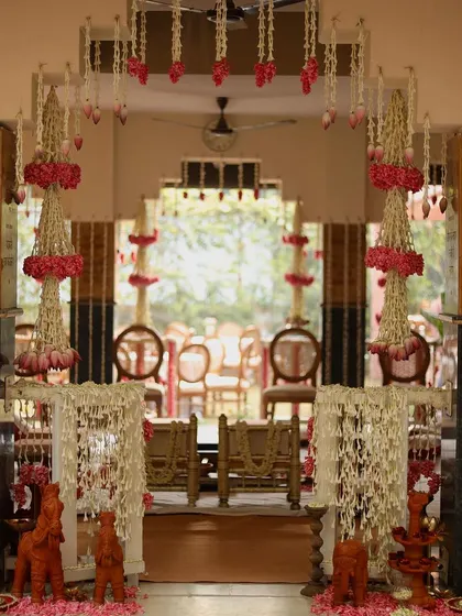 The entrance to the wedding ceremony space, framed by intricate hanging floral arrangements made of jasmine and pink carnations. Terracotta horses stand guard, adding a traditional touch.