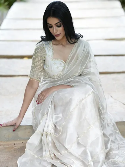 A seated pose in the white tissue silk saree, showing the beautiful fall of the fabric and the intricate details.