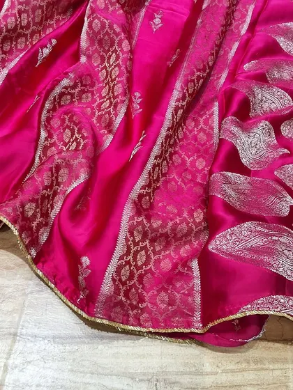 A vibrant pink soft silk saree with beautiful silver zari work. The combination of paisley motifs and geometric patterns makes it a standout piece from our festive collection.