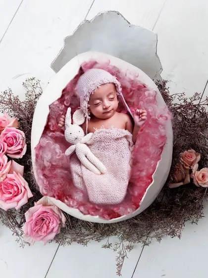 A delicate and creative newborn photo, with the baby nestled inside a cracked egg prop, surrounded by soft pink roses. This conceptual shoot is perfect for celebrating a new beginning.