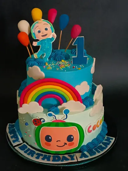 A grand two-tiered Cocomelon cake, complete with a rainbow, balloons, and the whole Cocomelon family for a very special first birthday.