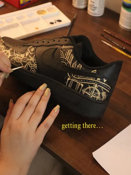 One brushstroke at a time. Here's a look at the process of painting a detailed city skyline and travel-themed icons onto a pair of black Nike Air Force 1s.