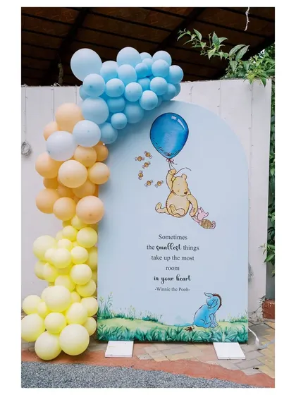 A beautiful arched backdrop featuring a classic illustration of Winnie the Pooh and Piglet, complete with a heartwarming quote. The pastel balloon garland adds a soft, celebratory touch.