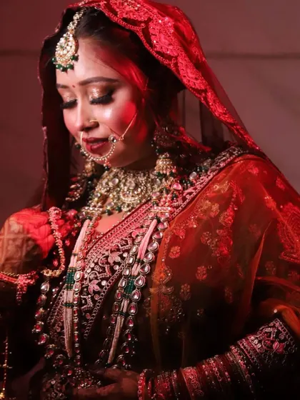 An artistic shot of the bride under a red light, highlighting the rich tones of her lehenga and the dramatic effect of her makeup.