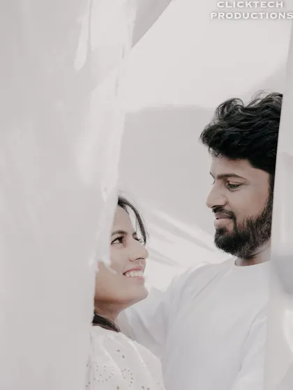 A soft and dreamy close-up of a couple looking at each other, framed by a sheer white curtain.