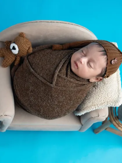 This little gentleman is sleeping so soundly on a miniature sofa. The brown knit wrap and tiny teddy bear add to the cozy and adorable scene.
