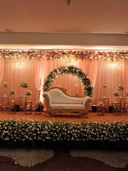 A beautiful indoor reception stage with a floral semi-arch. The elegant chaise lounge and candle-lit stands create a romantic and intimate setting.
