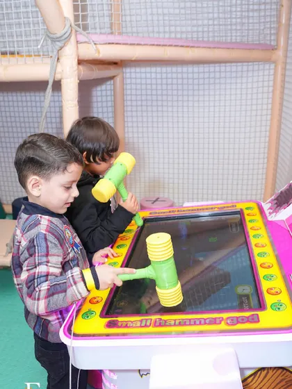 Two boys team up to play the "Small Hammer God" arcade game, testing their reflexes.