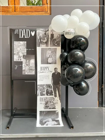 A Father's Day gift that's a walk down memory lane. This stand features a long scroll of black and white family photos, complemented by a simple black and white balloon garland.