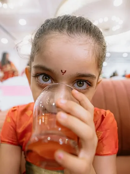 A close-up shot of a young guest enjoying a drink. Her wide, curious eyes looking directly at the camera make for a captivating and authentic portrait.
