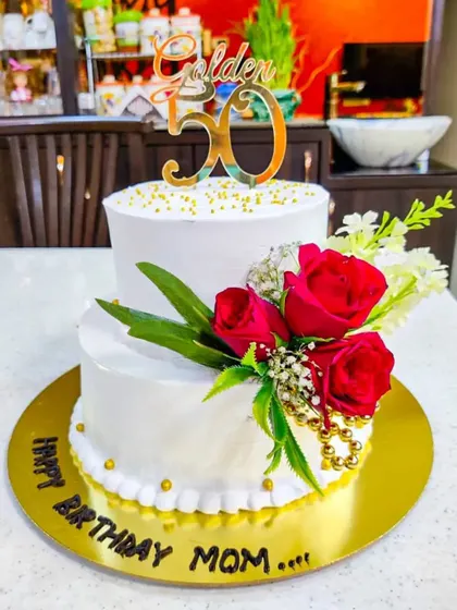 A beautiful two-tier cake for a mom's golden 50th birthday. The simple white design is elevated by a cascade of fresh red roses, creating a look of timeless elegance.