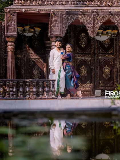 A beautiful reflection shot of the couple in traditional attire by the water, with ornate doors in the background.