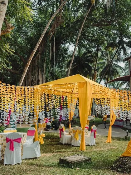 A dreamy outdoor Mehendi and Haldi space in Goa. We used colorful drapes and strings of marigolds to create a canopy, with fabric-wrapped palm trees adding to the festive, tropical vibe.