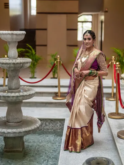 A full-length portrait of the bride by an elegant fountain. This shot captures her complete look, from the rich colors of her saree to her confident and happy posture.