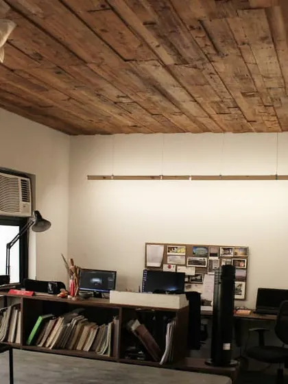 The interior of a studio space featuring a ceiling clad in reclaimed wood. This design choice adds texture and warmth, contrasting with the clean white walls and modern furniture to create a layered and inviting work environment.