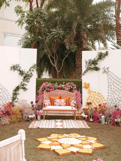 A wide shot of the 'Hall of Flowers' Haldi setup. The lush green lawn is contrasted with bursts of pink, orange, and yellow, creating a stunning visual spectacle.