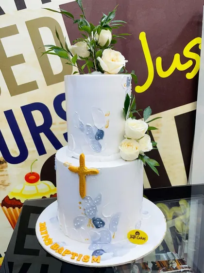 A beautiful 5kg two-tiered white cake for a baptism, decorated with a painted texture, a golden cross, and fresh white roses.