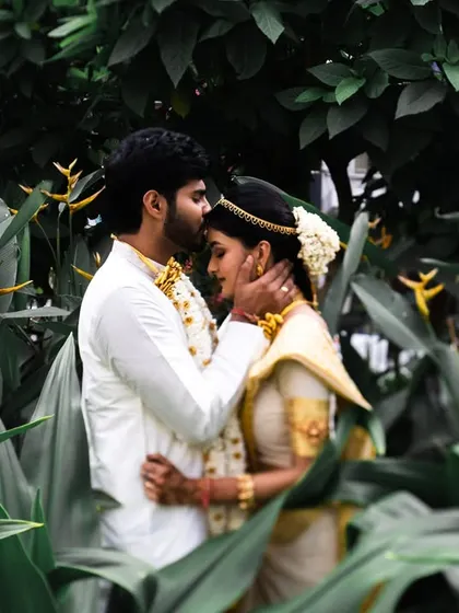 A tender forehead kiss, framed by lush green leaves. This is a classic, intimate shot that feels very private and romantic.