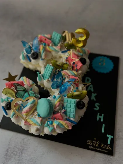 This number 3 cake has a whimsical, fairy-garden feel. It's decorated with pastel buttercream, edible butterflies, macarons, marshmallows, and fresh kiwi slices for a light and colorful celebration cake.