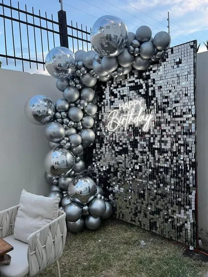 A glamorous birthday photo corner with a silver sequin wall and a cascade of silver and chrome balloons.