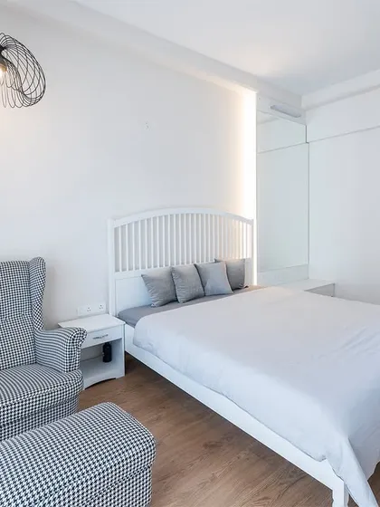 A minimalist master bedroom where simplicity reigns. The all-white theme is complemented by a statement pendant light and a comfortable armchair, creating a serene and clutter-free environment.