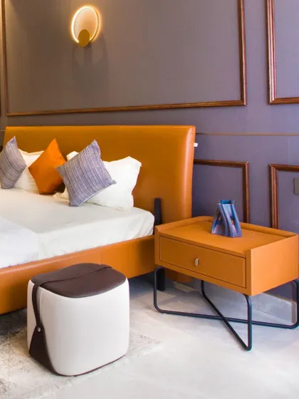 A contemporary bedroom with a bold orange leatherette bed. The matching bedside table has a sleek, minimalist design with a single drawer and black metal legs.
