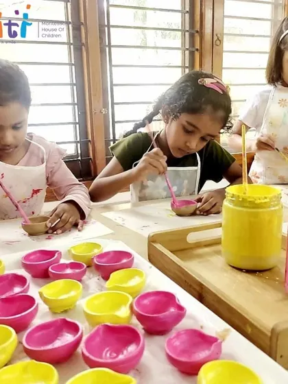 Girls concentrate on painting their handmade diyas with bright pink and yellow colors. This activity develops their fine motor skills and artistic expression.