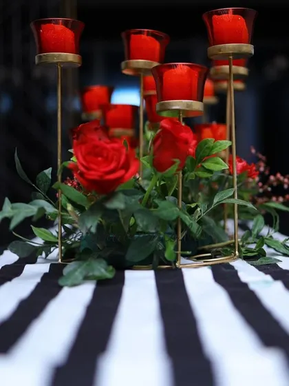 A chic and modern centerpiece for a 40th birthday party. Red roses and candles in red glass holders are arranged on a black and white striped table runner, creating a bold and sophisticated look.