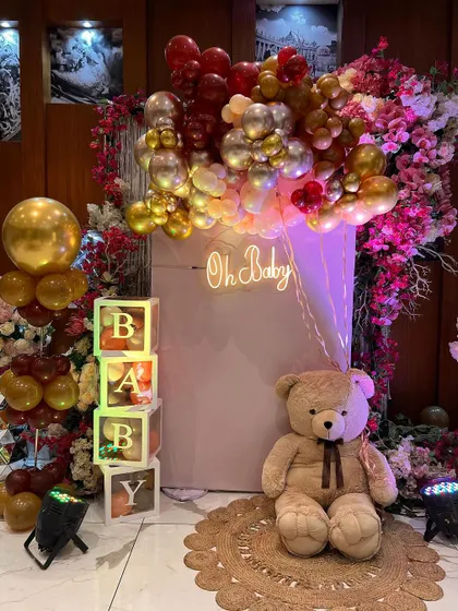 A beautiful photo corner for a baby shower with an "Oh Baby" neon sign, a large teddy bear, and a mix of floral and balloon decor.