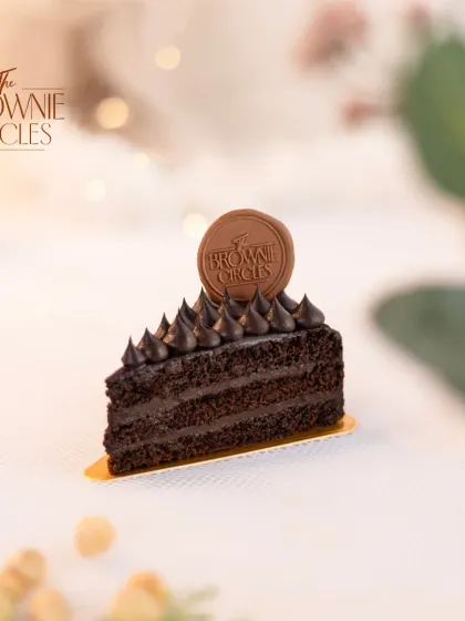 A slice of my Chocolate Ganache pastry. You can see the rich layers of chocolate cake and creamy ganache, topped with our signature chocolate logo.