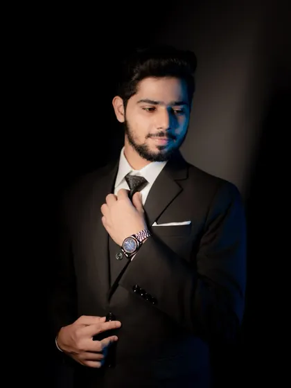 A stylish portrait of the groom-to-be adjusting his tie, with dramatic lighting highlighting his features.