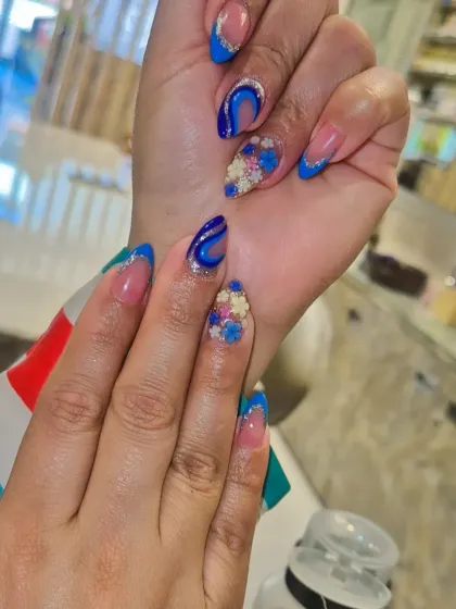 A modern twist on the classic French manicure. This design features a bold blue French tip, silver glitter accents, abstract swirls, and intricate 3D floral embellishments on an almond-shaped nail. It’s a great example of how I combine multiple techniques into one cohesive, artistic set.