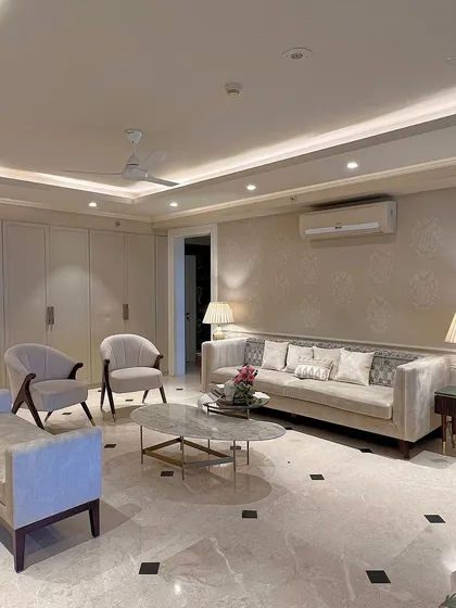 A formal living room designed with bespoke elegance. The space features a classic sofa, matching armchairs, and a daybed, all unified by a soft, neutral color scheme and sophisticated stencil art on the wall.