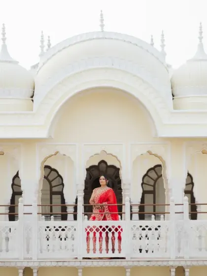 The bride stands on the palace balcony, a picture of grace and beauty. This wide shot captures both her stunning look and the magnificent architecture of the venue.