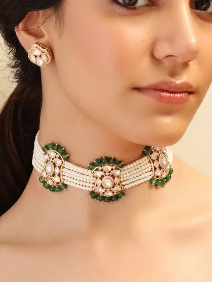 A classic pearl choker interspersed with floral motifs made of polki and green enamel, paired with simple matching studs.