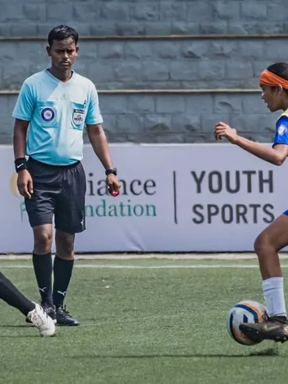 An action shot from the Reliance Foundation Young Champs Football Cup, with our player skillfully dribbling past a defender under the watchful eye of the referee.